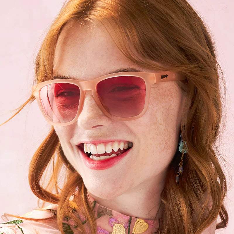 Blush pink sunglasses with gradient lenses on person smiling, Don't Make Me Blush.