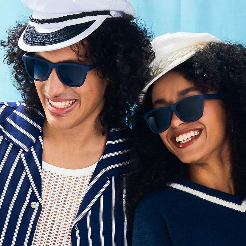 Two people wearing sailor hats and sunglasses, smiling.