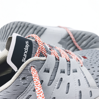 Close-up of grey sundays running shoe with red laces and breathable upper design.
