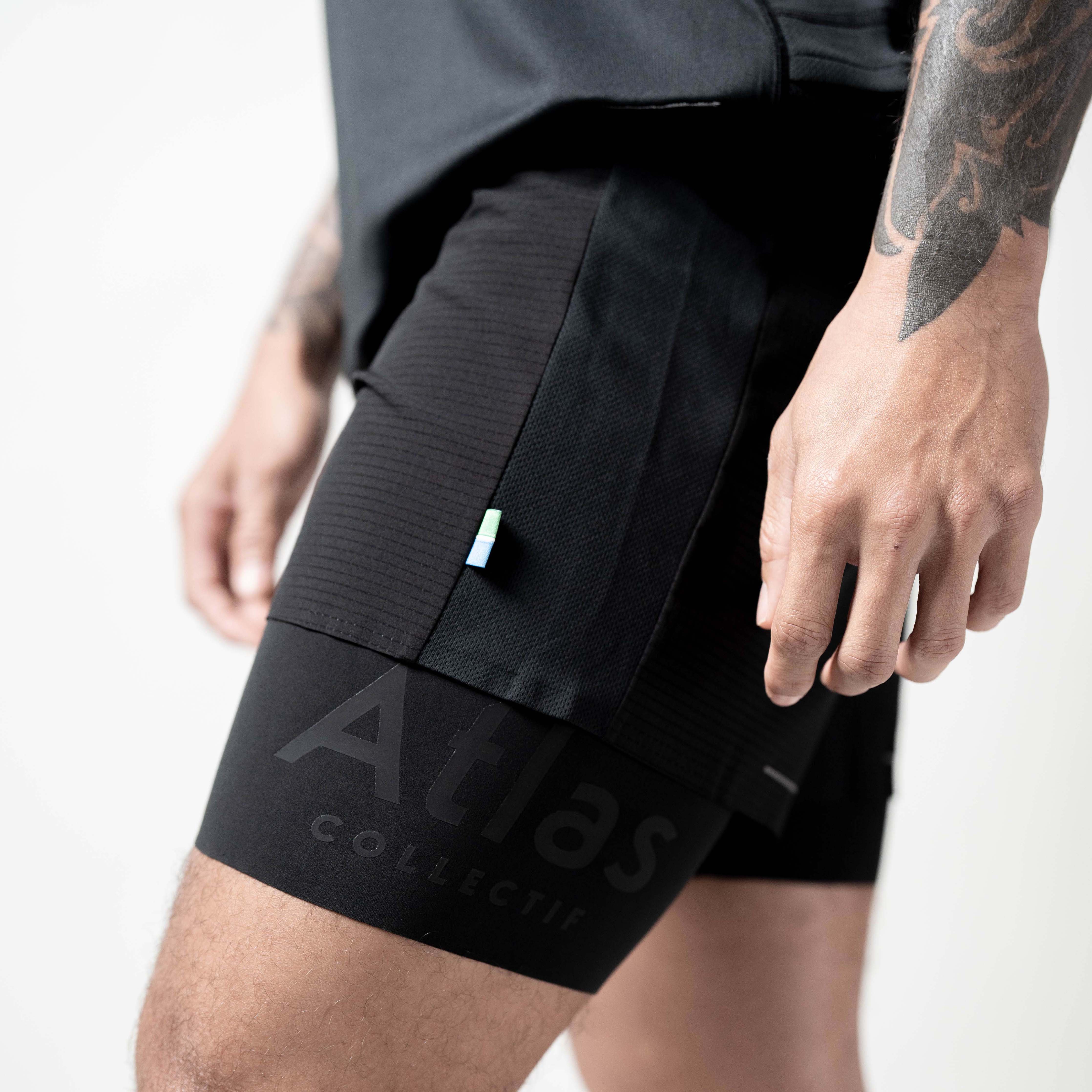 Black performance 2-in-1 running shorts, tight fit, crafted from recycled materials, featuring moisture-wicking and quick-drying properties, with a reflective detail and back zip pocket.