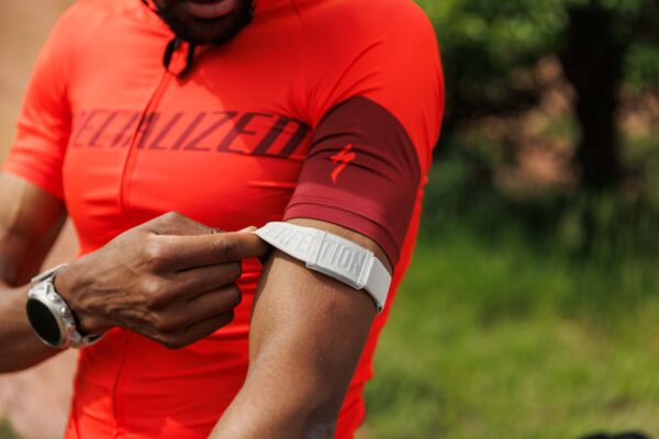 COROS HR Monitor - ARM BAND worn by a cyclist in a red jersey, showcasing comfortable fit and easy adjustment.