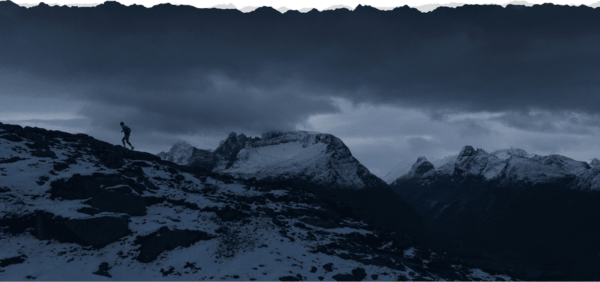 Trail runner on a snowy mountain under cloudy sky.
