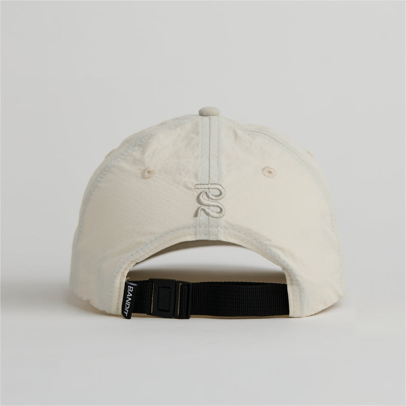 Cream nylon dad hat with adjustable webbing, durable ripstop fabric, and embroidered logos.